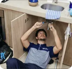 Um homem está deitado no chão consertando uma pia na cozinha.