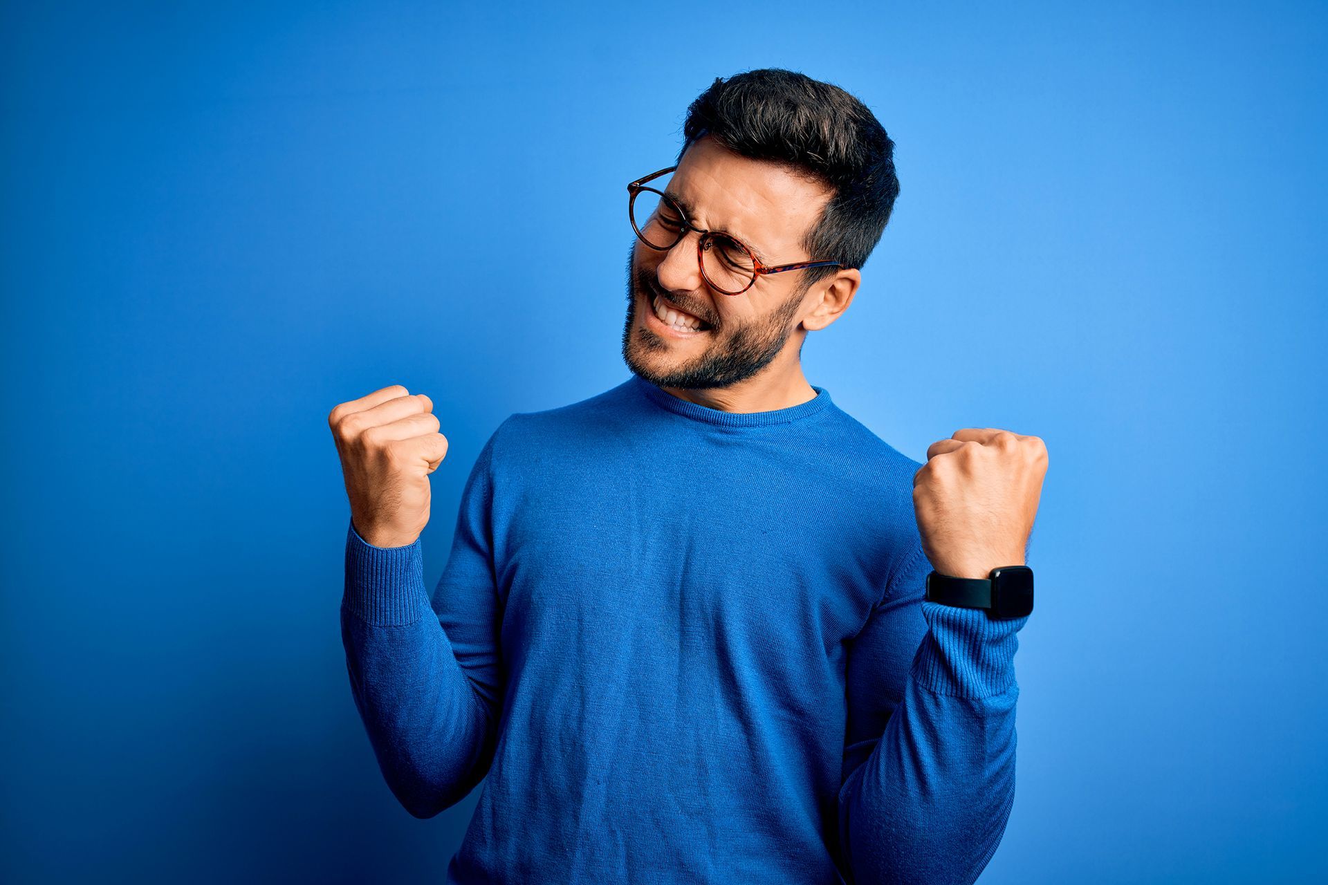 Um homem usando óculos e um suéter azul está levantando o punho no ar.