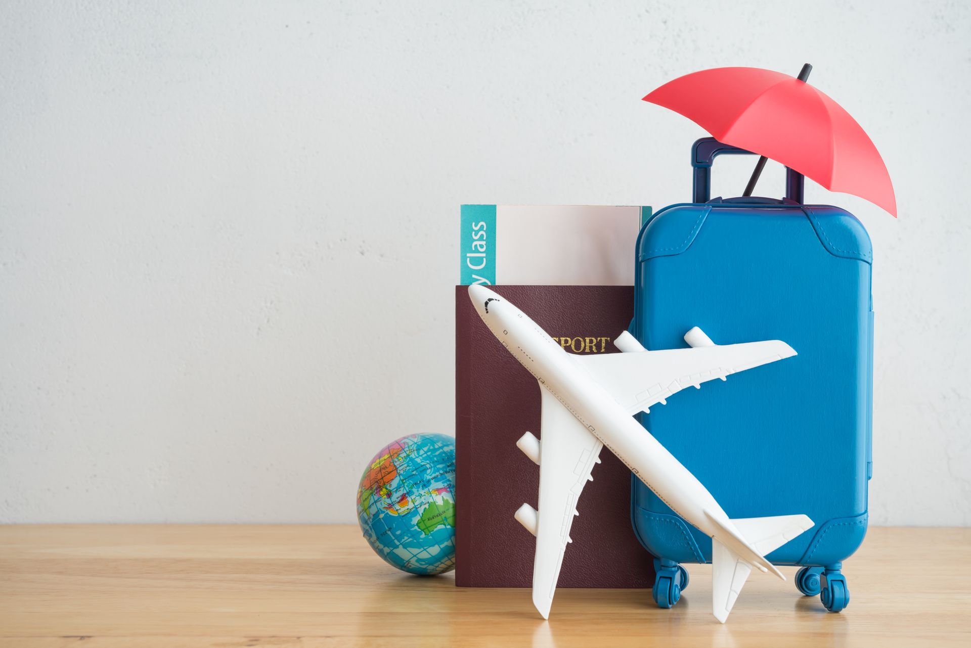 Um avião de brinquedo, mala, passaporte, globo e guarda-chuva em uma mesa de madeira.
