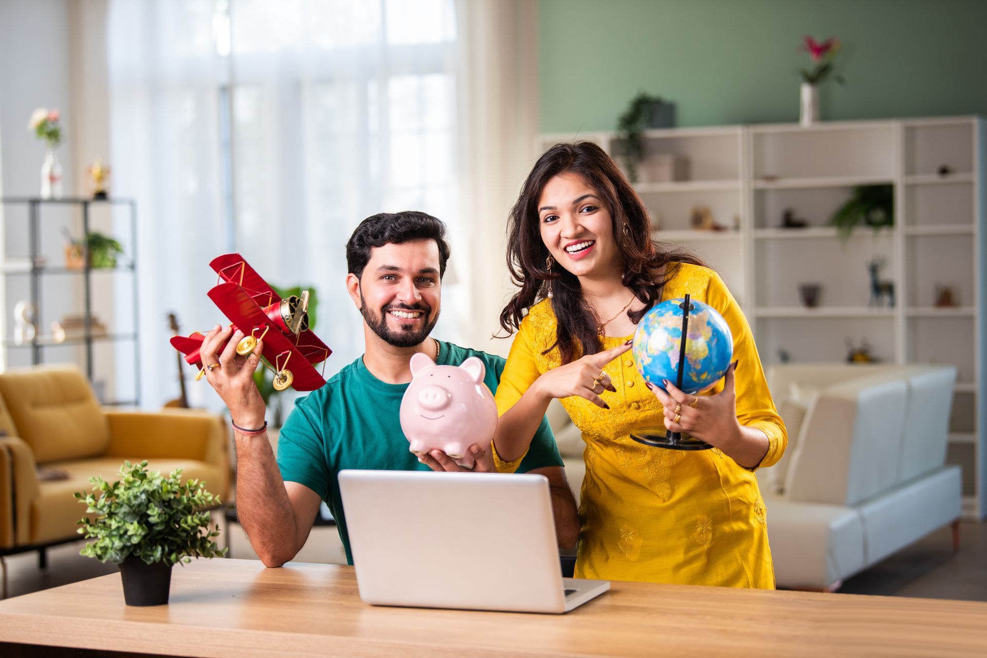 Um homem e uma mulher estão sentados à mesa com um laptop e um cofrinho.