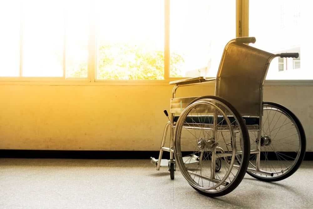 Uma cadeira de rodas vazia está sentada em frente a uma janela em uma sala vazia.