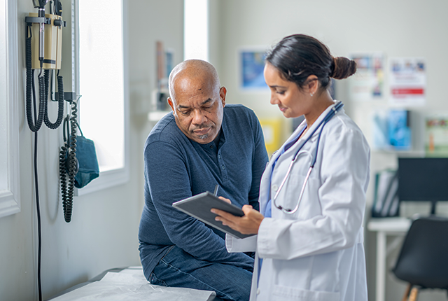 A doctor is talking to a patient while looking at a tablet.