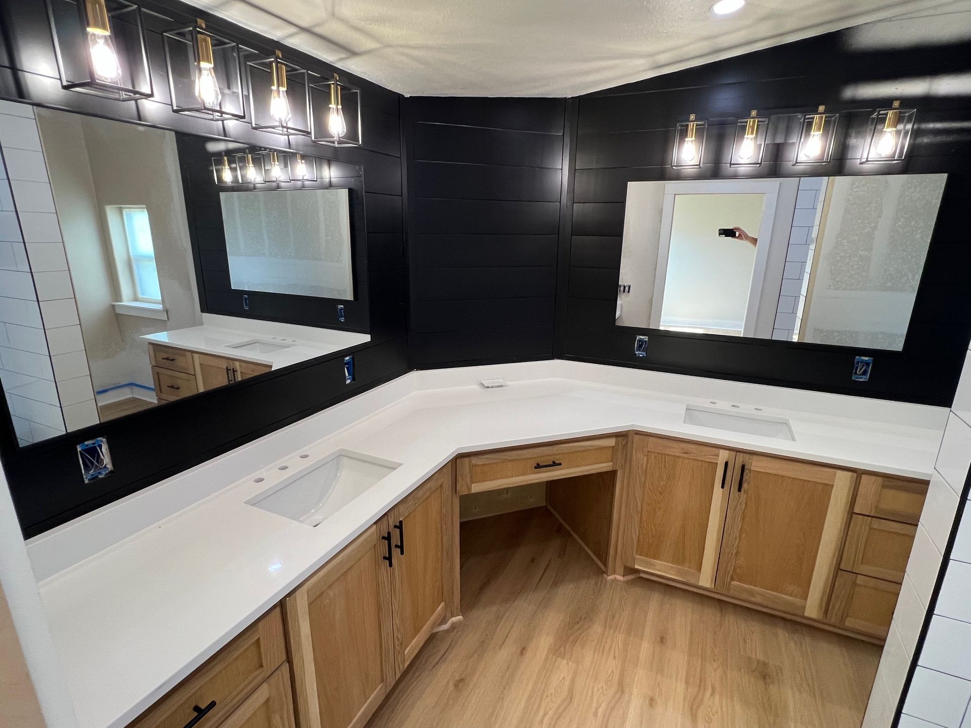 Bathroom with black accent wall, light wood cabinets, and white countertop. Two mirrors with light fixtures.