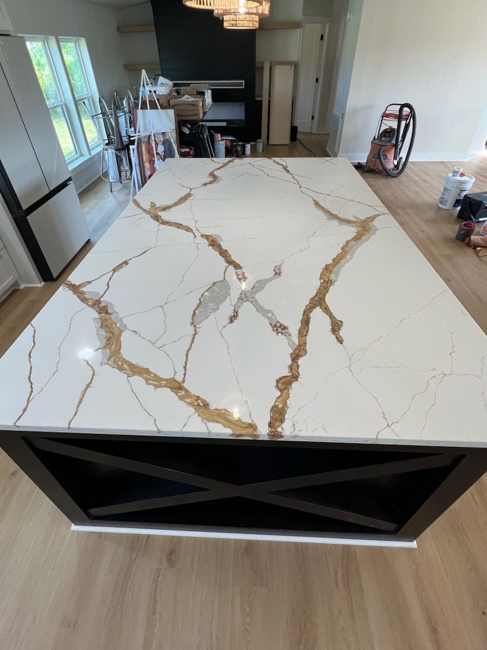 Large kitchen island with white countertop, gold veining, dark base, and wood flooring.