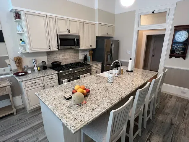 Kitchen with island seating, granite countertops, stainless steel appliances, and off-white cabinets.