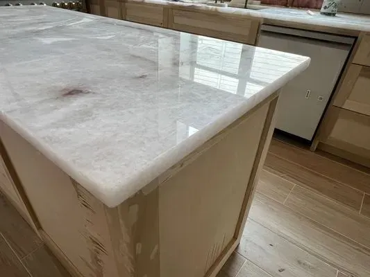 Close-up of a kitchen island with a glossy, light-colored countertop. Cream-colored cabinets are visible.
