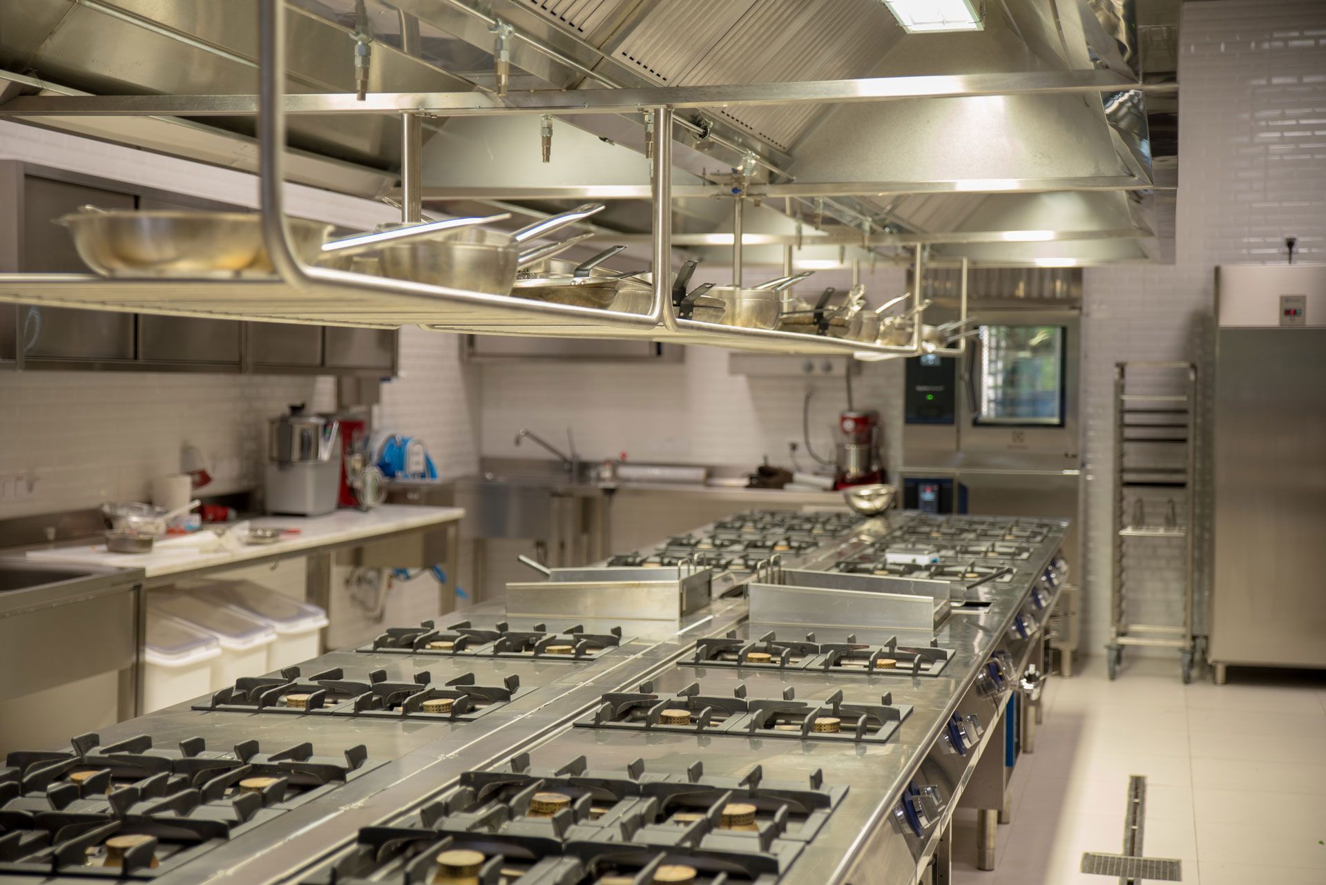 Modern commercial kitchen with rows of gas stoves, stainless steel counters, and overhead ventilation
