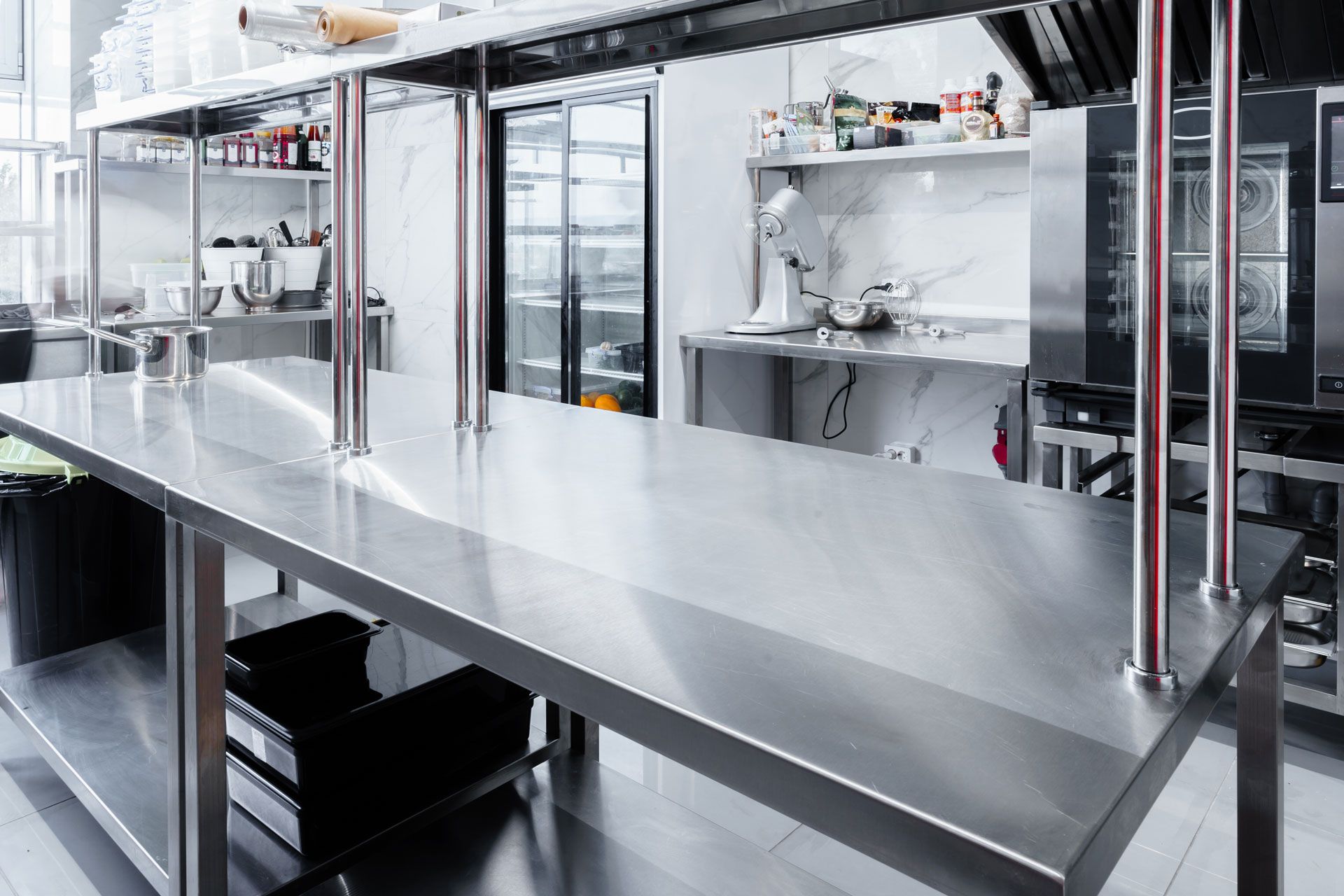 Empty stainless-steel commercial kitchen with long prep counter and shelves of dishes and utensils