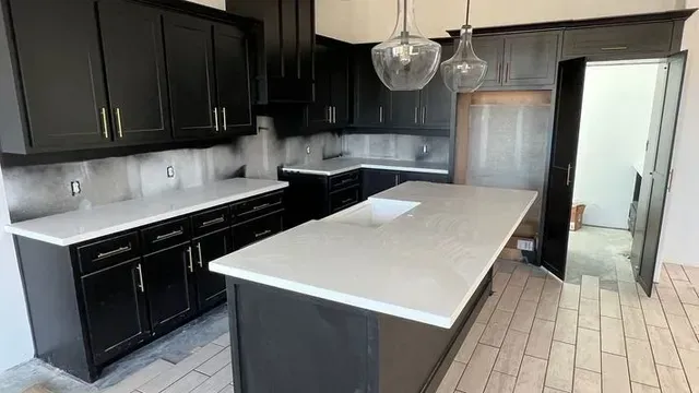 Dark kitchen cabinets with light countertops and an island. Two pendant lights hang above.