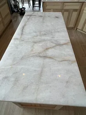 White and tan marble countertop on a kitchen island. Sunlight reflects off the smooth surface.