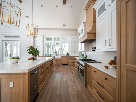 Bright modern kitchen with wood floors, white cabinets, island, and large windows overlooking greenery