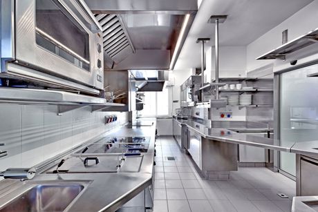 Bright stainless-steel commercial kitchen with ovens, counters, and shelves, no people