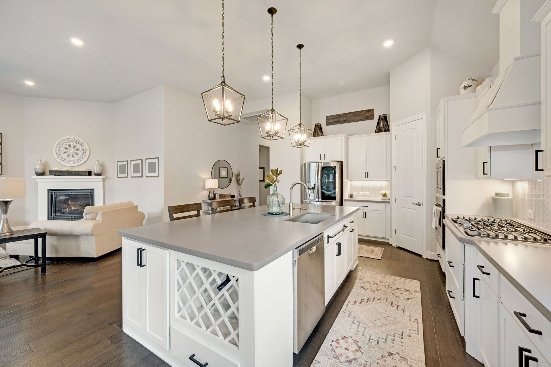 Bright modern kitchen with white cabinets, island, pendant lights, and adjacent living room fireplace