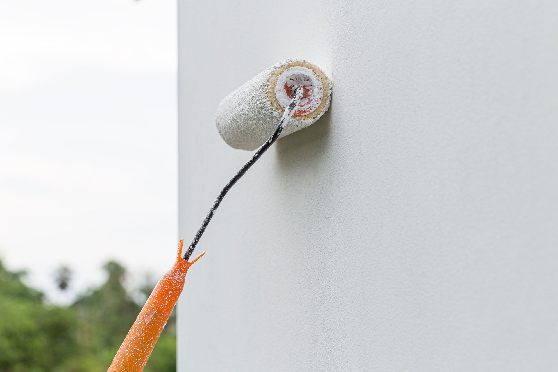 Paint roller applying white paint to a wall.