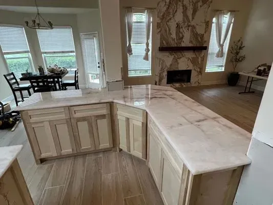 Kitchen with light-colored cabinets, marble countertops, and a stone fireplace in the background.