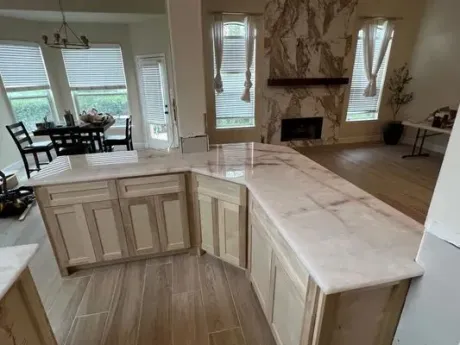 Bright kitchen with white cabinets and island, opening to a dining and living area with large windows.