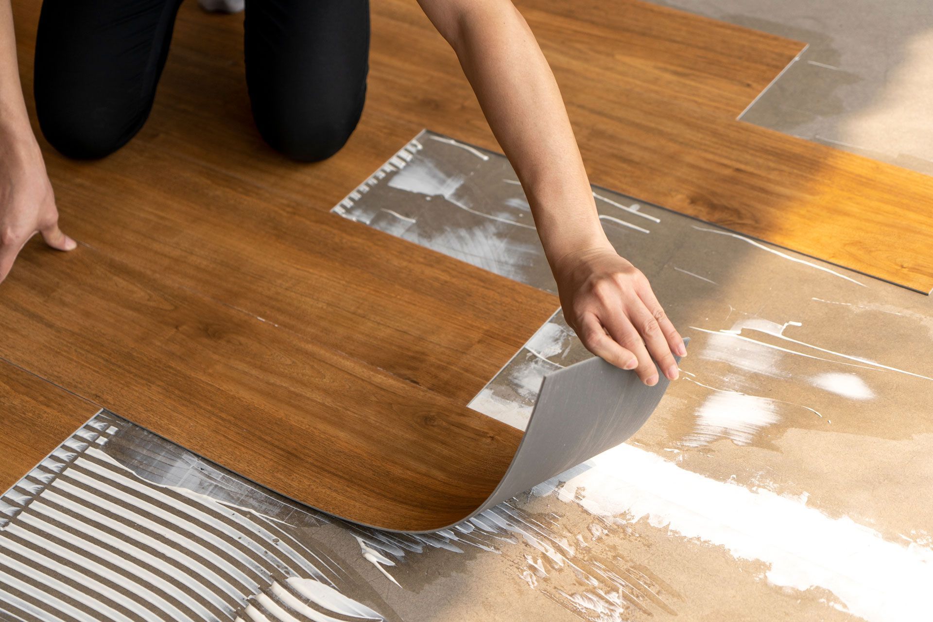 Person installing wood-look vinyl flooring, applying adhesive to subfloor.