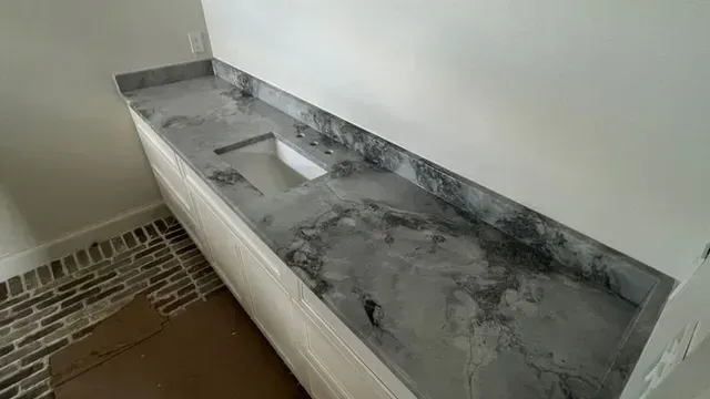 Gray marble countertop on white cabinets in a room with a patterned brick-like floor.