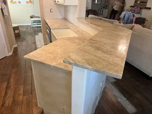Beige granite countertops on a kitchen island, contrasting with dark wood floors.