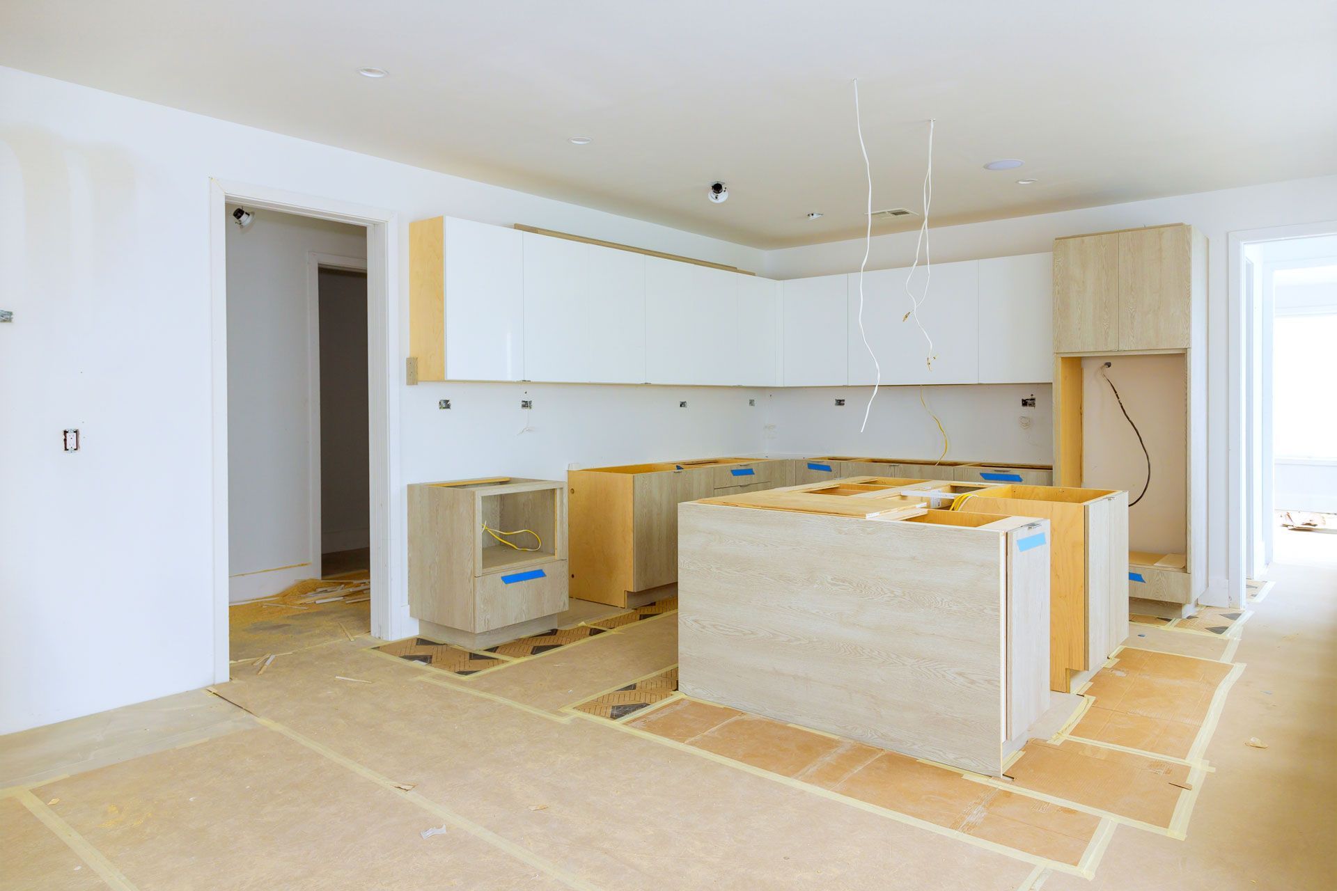 Unfinished kitchen with white cabinets, bare floors, and appliances wrapped for renovation.