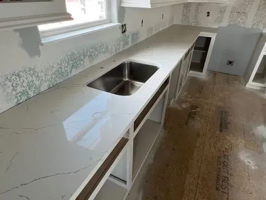 Kitchen countertop with stainless steel sink, cabinets, and partially finished backsplash, next to a window.