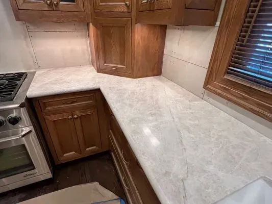 Kitchen countertop with marble-like pattern. Wooden cabinets below and above. A gas stove is visible on the left.