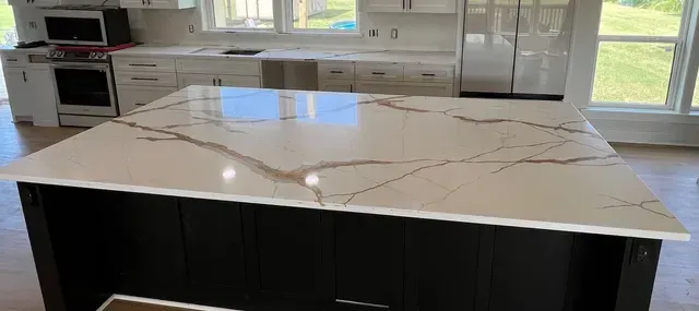Kitchen with white cabinets, dark island, and light countertops with brown veining.