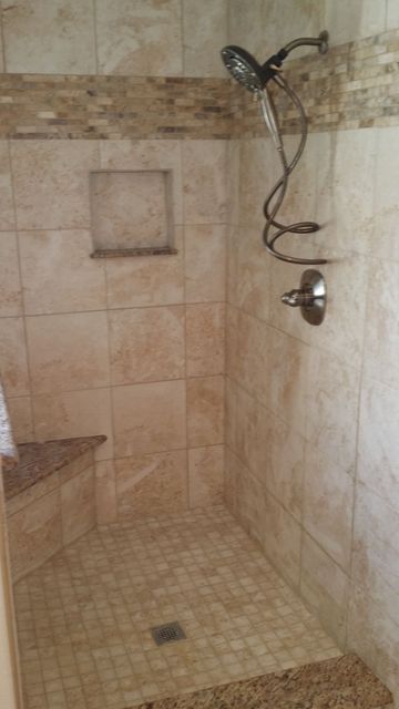 Shower with beige tile, built-in bench, decorative stone border, and showerhead.