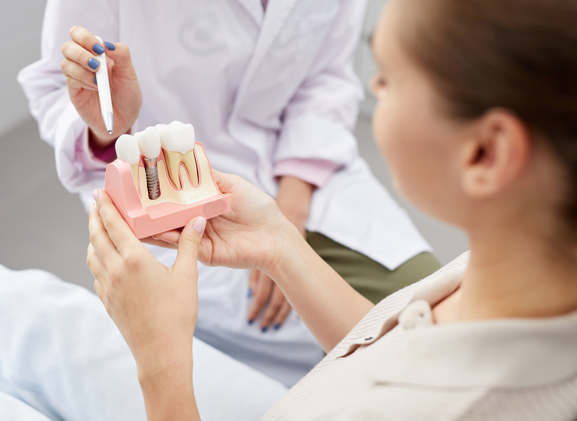 Dentist showing patient a tooth model, explaining dental procedure in office setting.