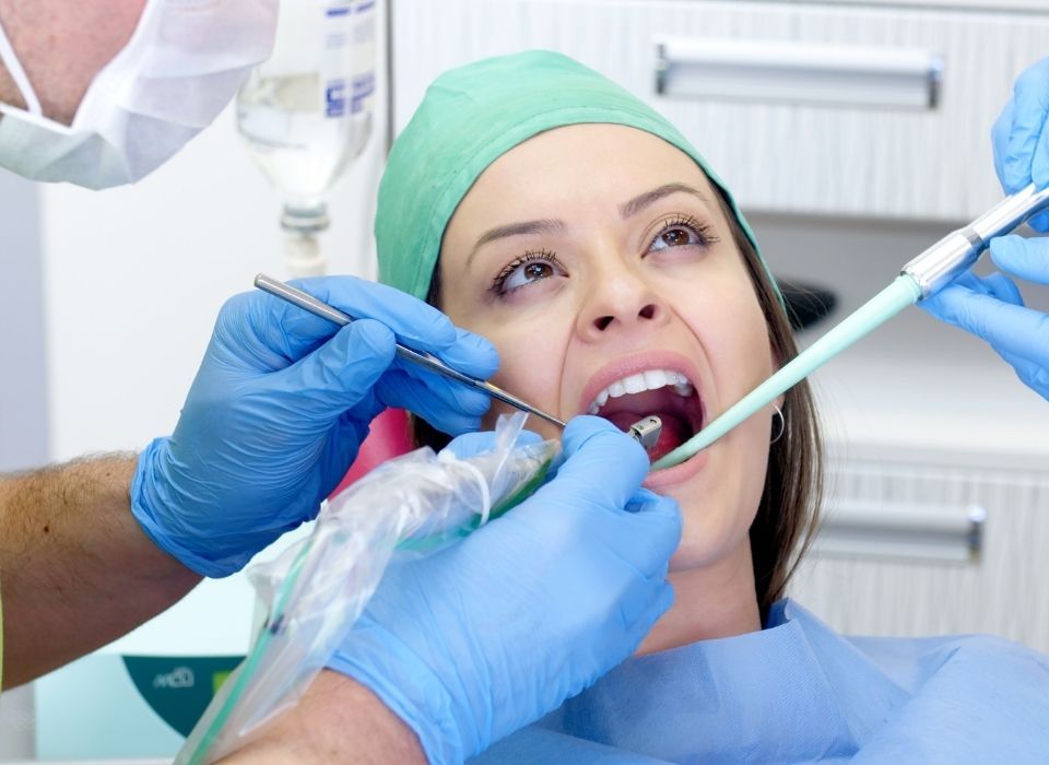 Woman in dental chair with mouth open, dental tools in use.