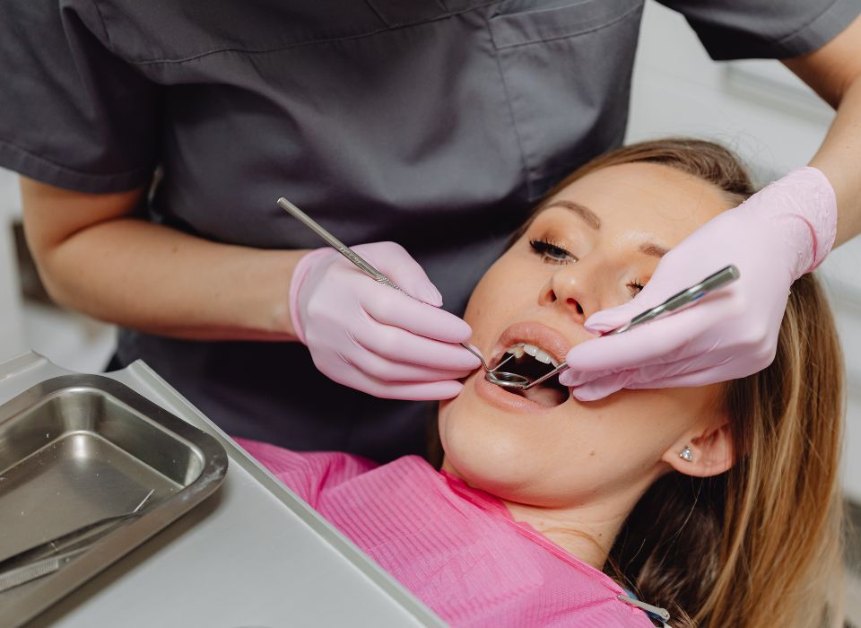 Woman in dentist chair, mouth open, receiving dental exam. Dentist in pink gloves holds instruments.