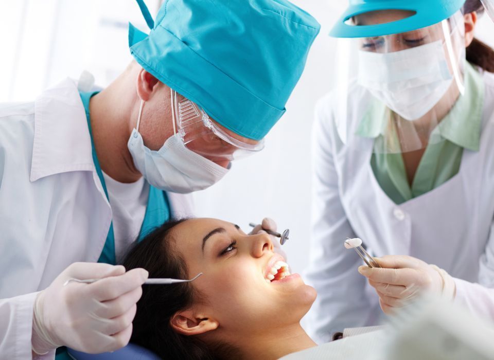 Dentist examining patient's teeth. Doctor and assistant in scrubs, masks, and gloves.