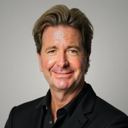 Portrait of a smiling man in a black suit against a light gray background