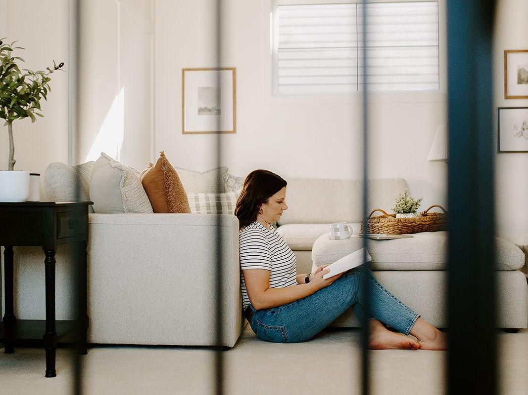 Megan Atamanik is sitting on the floor reading a book in a living room.