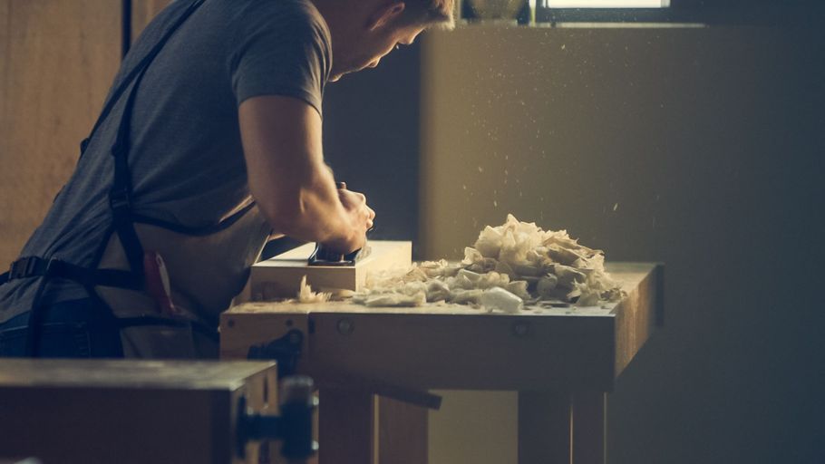 Person shaping clay at a pottery wheel beside a table piled with white clay in a dim studio