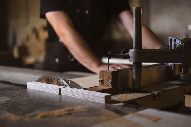 Woodworking clamp securing a piece of wood on a workshop table, with a person blurred in the background