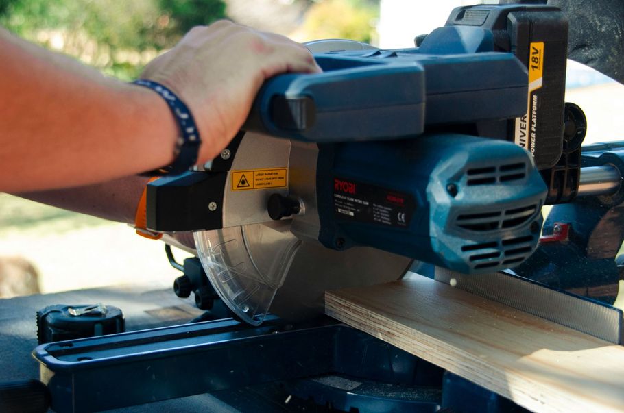 Hand holding a blue miter saw cutting a wooden board outdoors