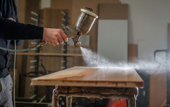 Person spray-painting a wooden board on a workbench in a workshop