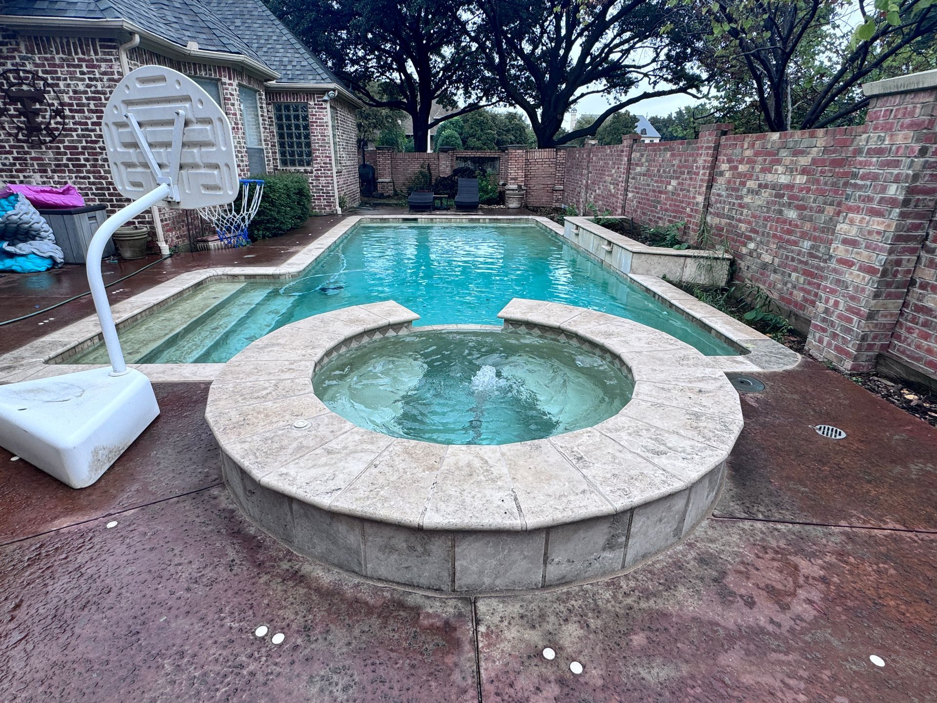 A basketball hoop is sitting next to a swimming pool.