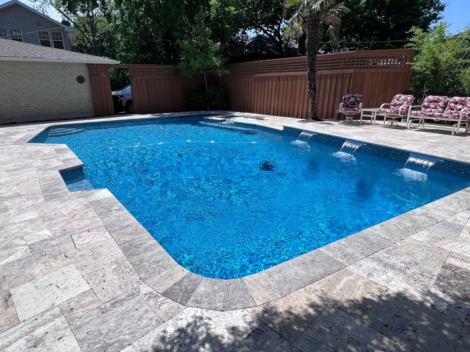 A large swimming pool is surrounded by a stone patio and a wooden fence.