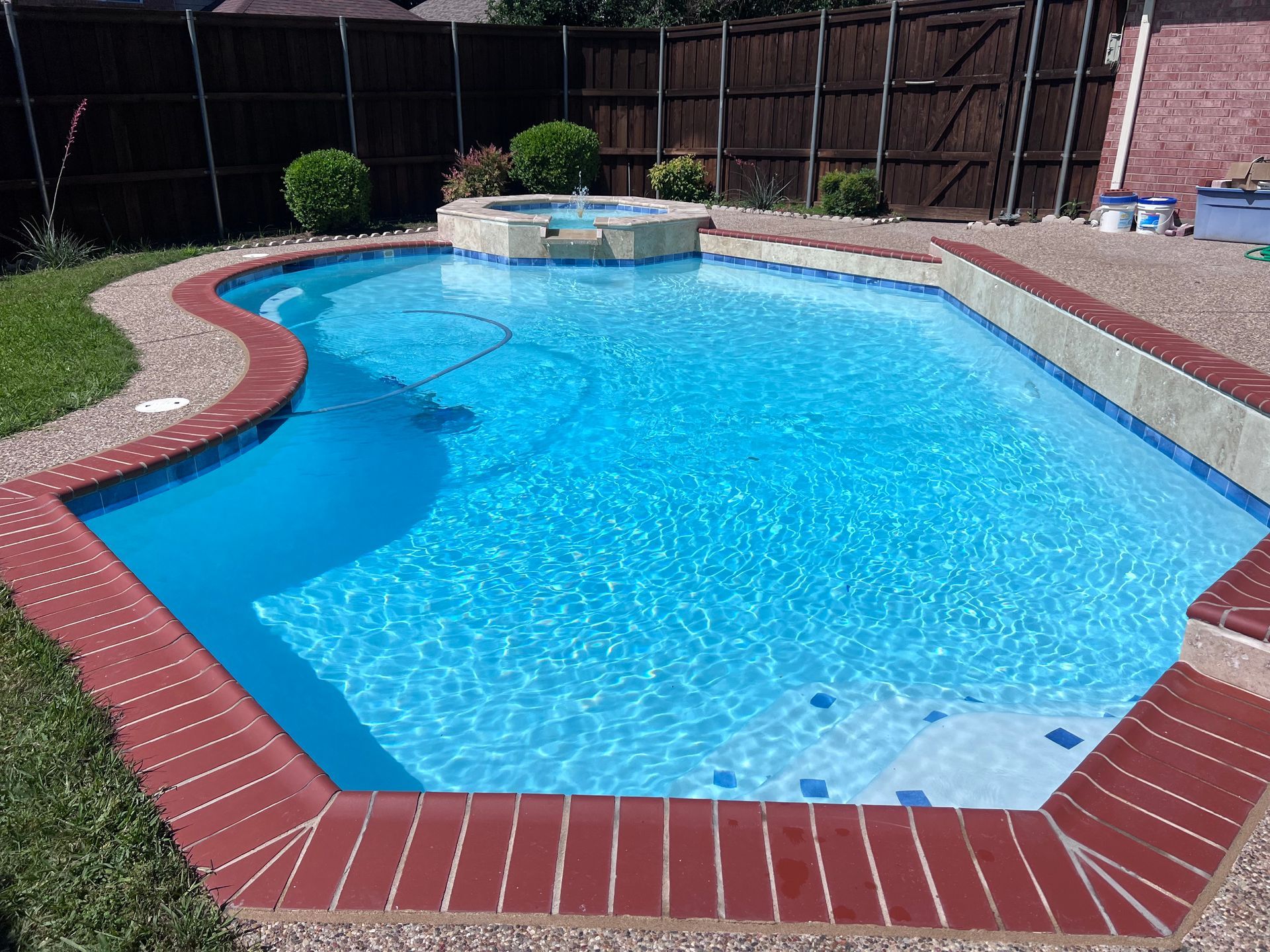A large swimming pool with a brick border and a fence in the background.