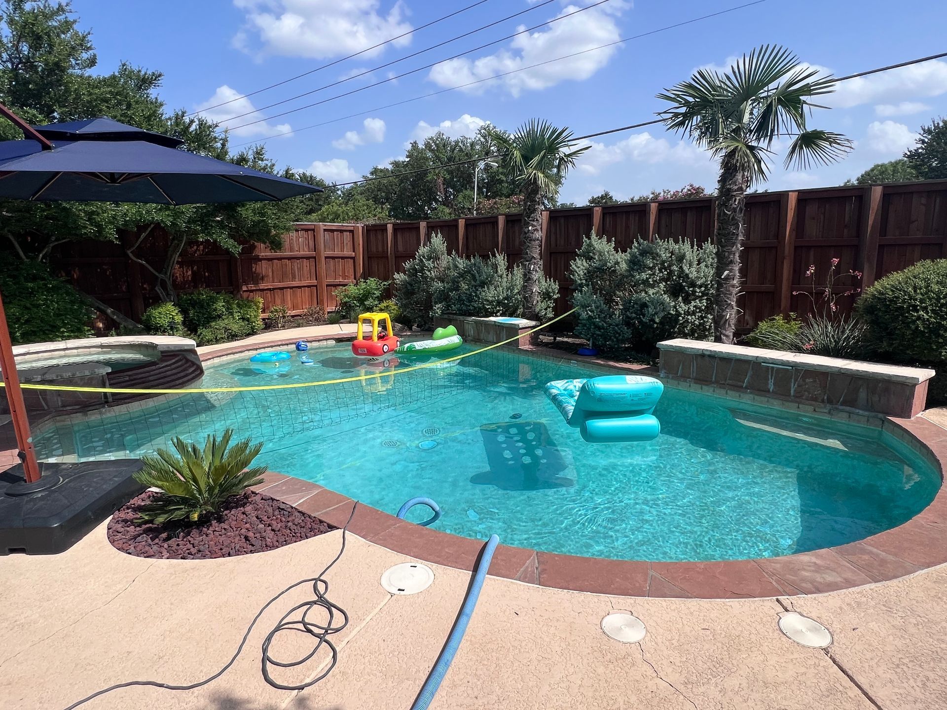 A large swimming pool with a blue umbrella in the backyard