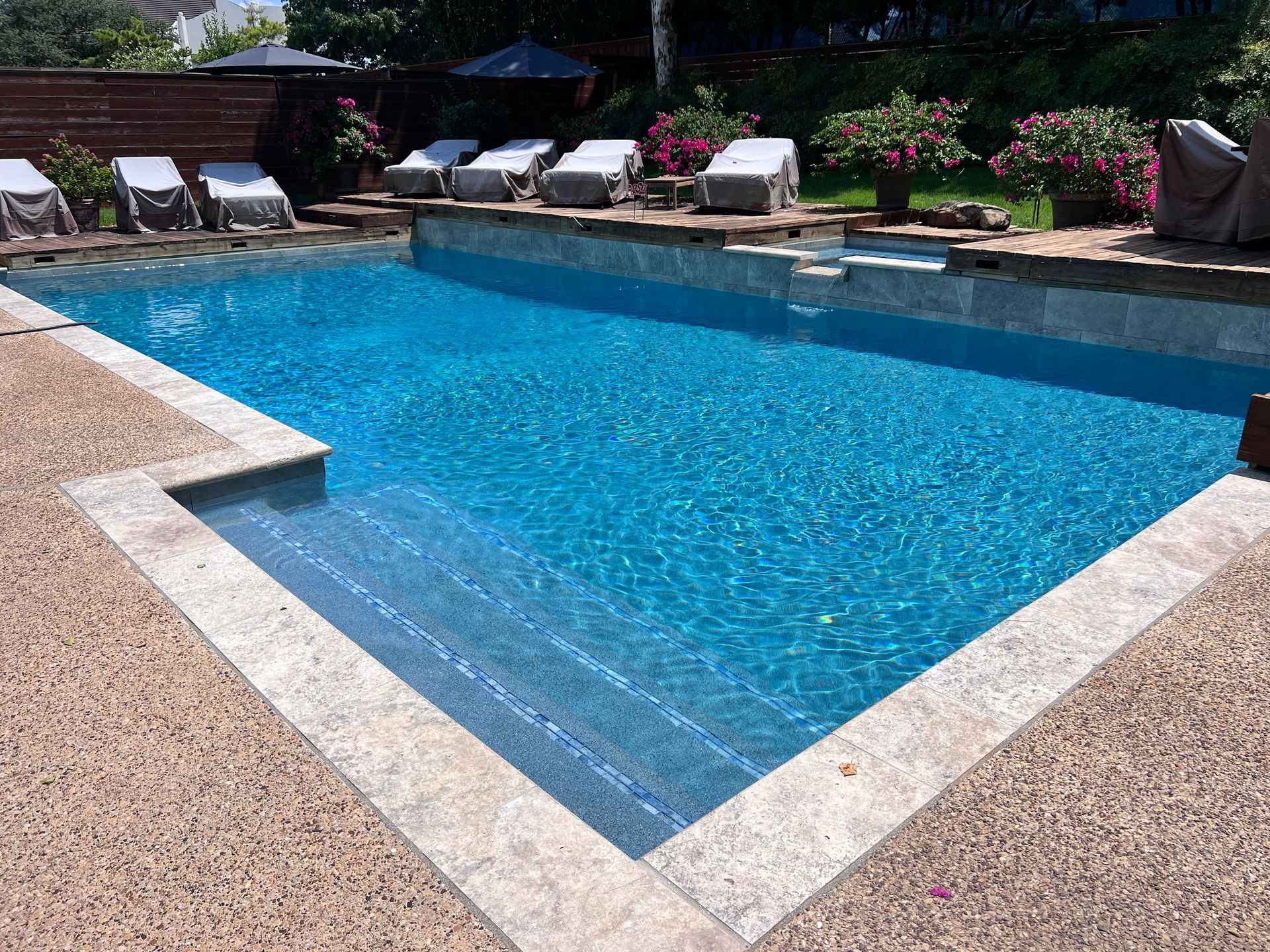 A large swimming pool surrounded by chairs and flowers in a backyard.