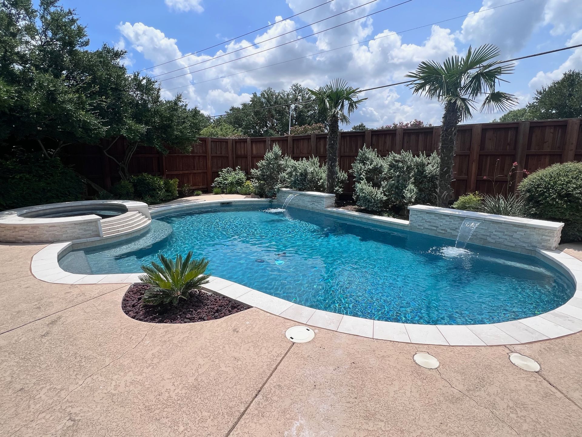 A large swimming pool with a waterfall in the backyard of a house.