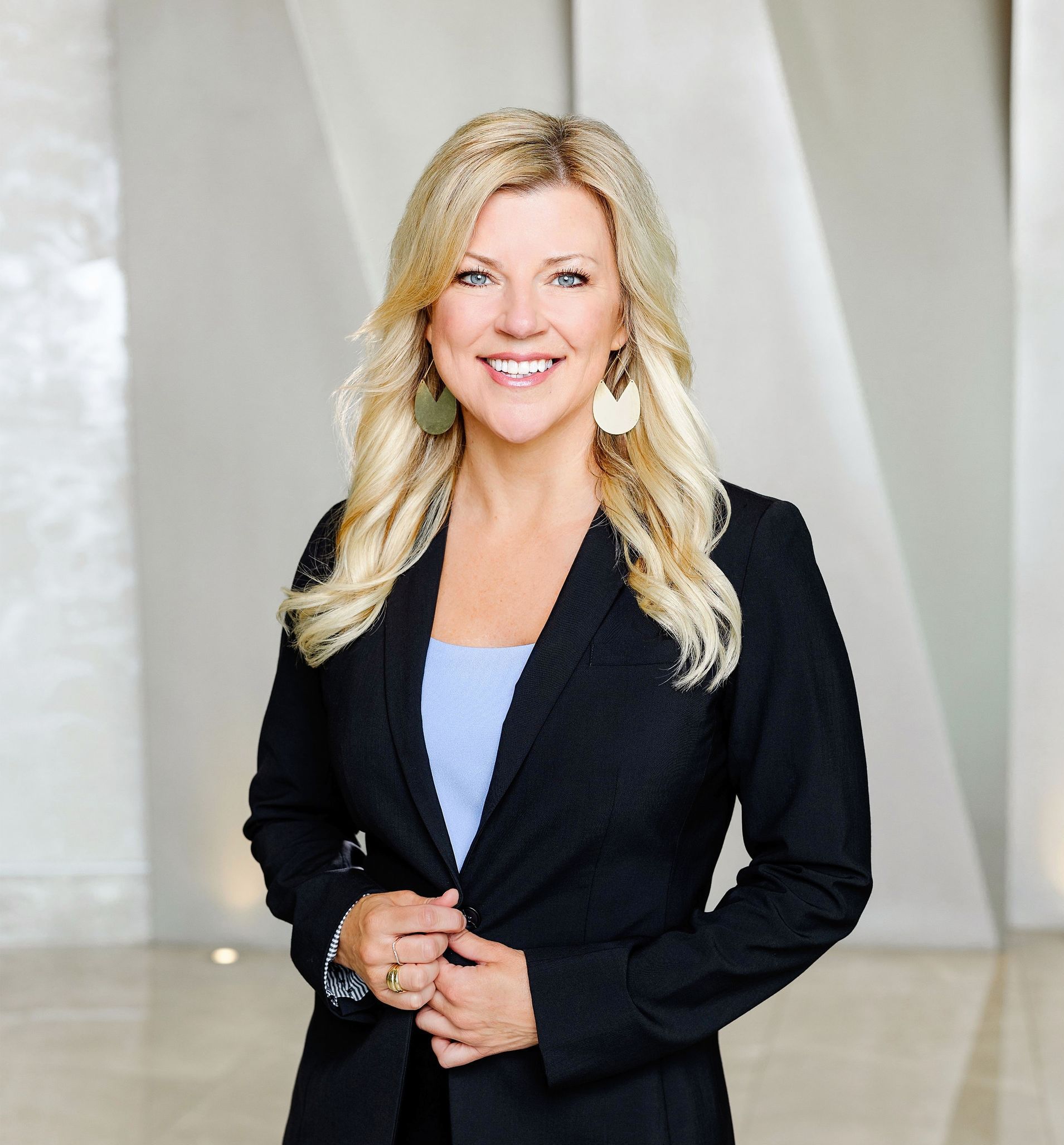 A woman wearing a black jacket and earrings is smiling for the camera.