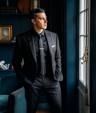 A man in a suit and tie is standing in front of a window.