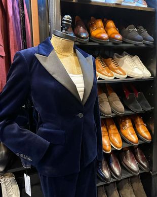 A mannequin is wearing a blue tuxedo in front of a shelf of shoes.