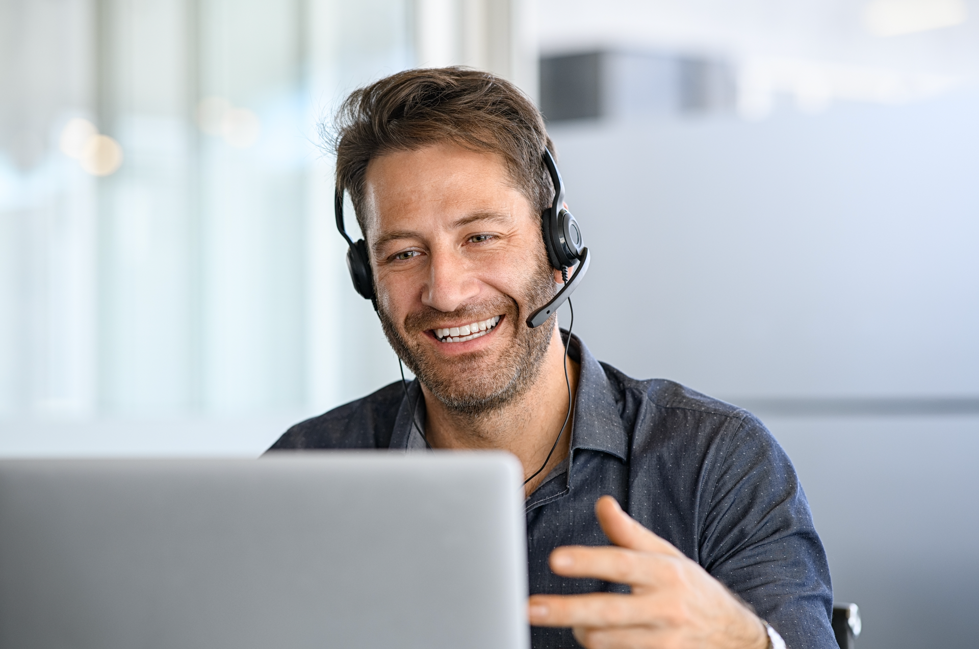 A man wearing a headset is sitting in front of a laptop computer.