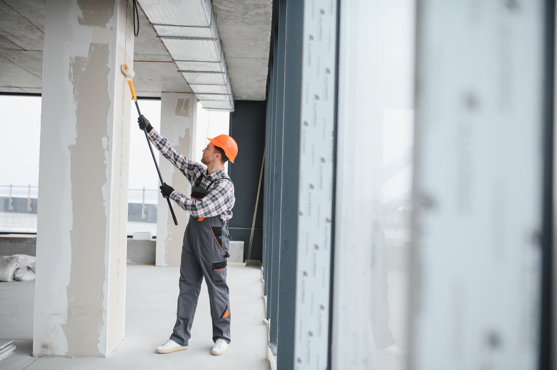 Worker in orange hard hat painting a ceiling beam inside a building under construction