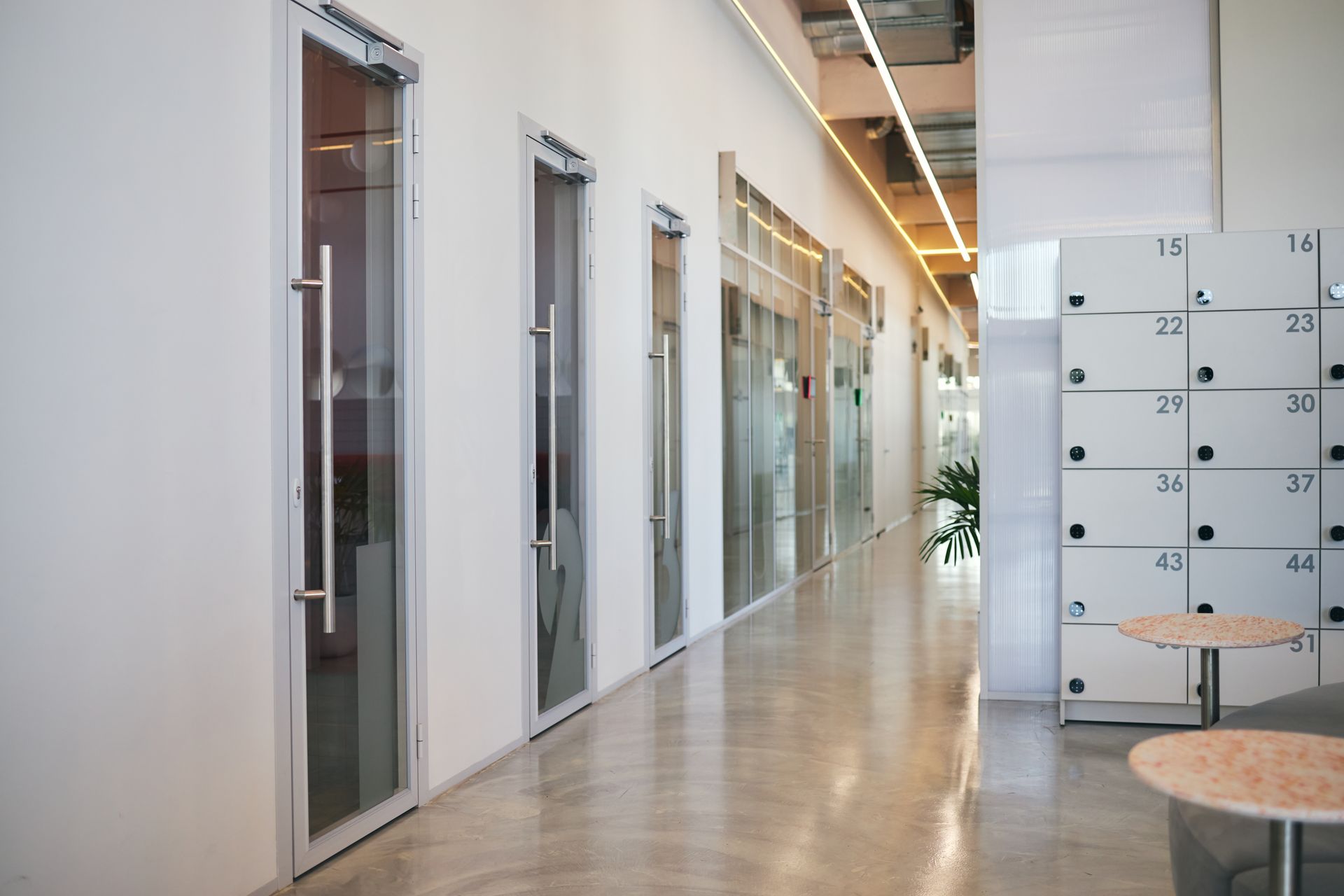 Modern office corridor with glass doors, lockers, and a polished floor Modern office corridor with glass doors, lockers, and a polished floor